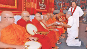 Gotha kneel down in front Buddist monks Mahinda standing பொருளாதார அரசியல் - தமிழ் மக்கள் கருத்தில் எடுக்கவேண்டிய தருணமிது- வேல்ஸ் இல் இருந்து அருஸ்